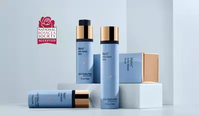 Four skinbetter science products—two tall pump bottles, one medium bottle with gold cap, and a small square jar—arranged on white and pale-blue geometric pedestals. A red 'National Rosacea Society Accepted' badge floats in the top left corner.