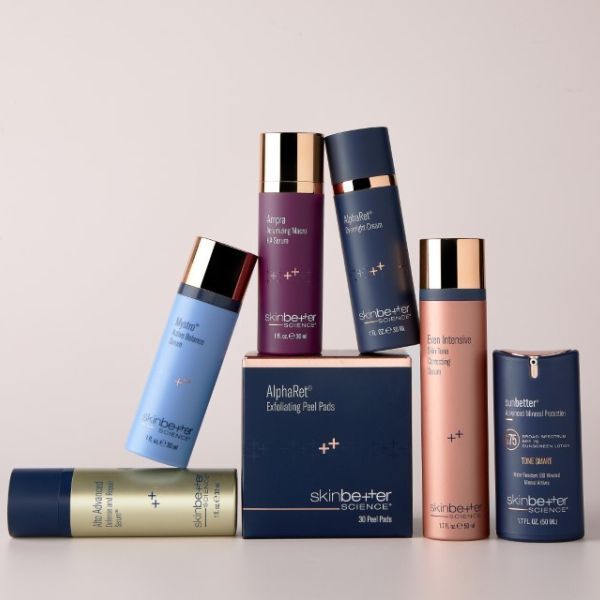 Four skinbetter science products—two tall pump bottles, one medium bottle with gold cap, and a small square jar—arranged on white and pale-blue geometric pedestals. A red 'National Rosacea Society Accepted' badge floats in the top left corner.